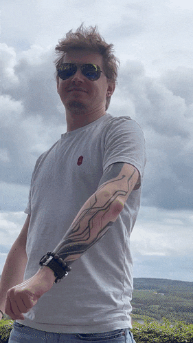a man wearing sunglasses and a white shirt has a tattoo on his arm
