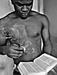 a shirtless man smoking a cigarette while reading a bible