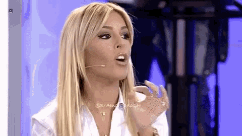 a woman with blonde hair and a white shirt is talking into a microphone .