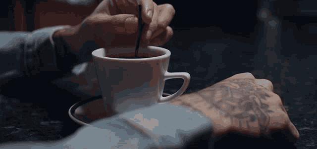 a person with a tattoo on their arm stirs a cup of coffee with a spoon