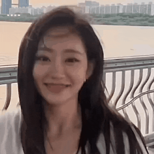 a close up of a woman 's face while sitting on a bench next to a body of water .