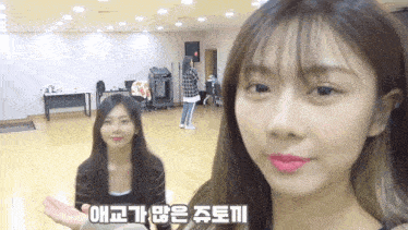 two girls are standing next to each other in a room . one of the girls is wearing pink lipstick .