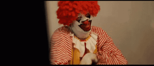 a clown in a red and white striped outfit is holding a banana .