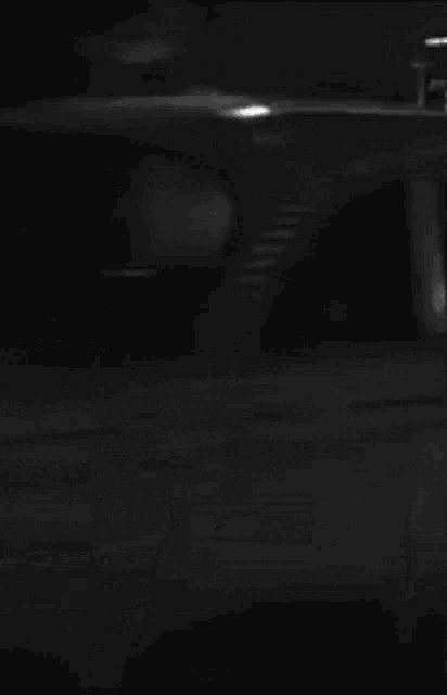 a black and white photo of a taxi cab driving down a street at night