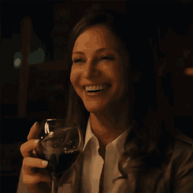 a woman holds a glass of red wine and smiles