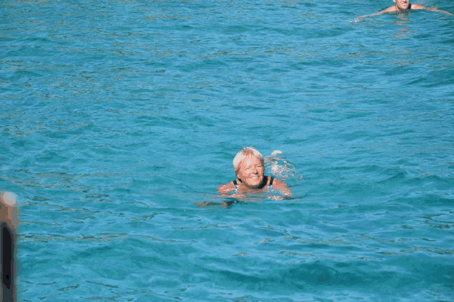 a woman is swimming in the ocean while another man looks on