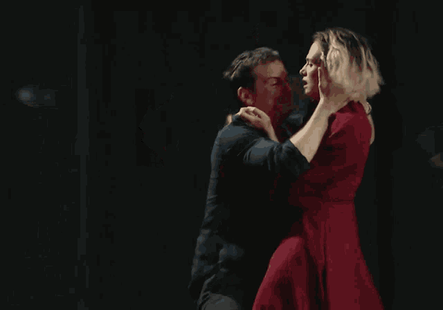 a woman in a red dress kisses a man in a blue shirt who is holding a newspaper