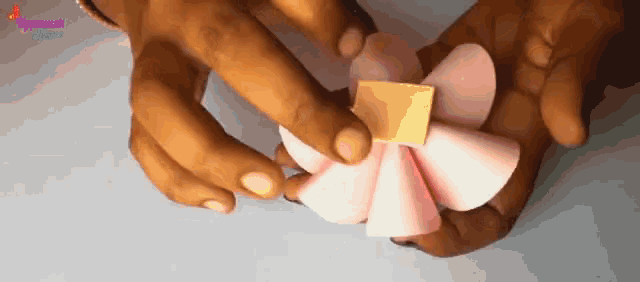a person is holding a pink and yellow paper flower in their hand .