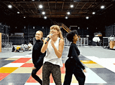 a woman singing into a microphone while two other women dance around her