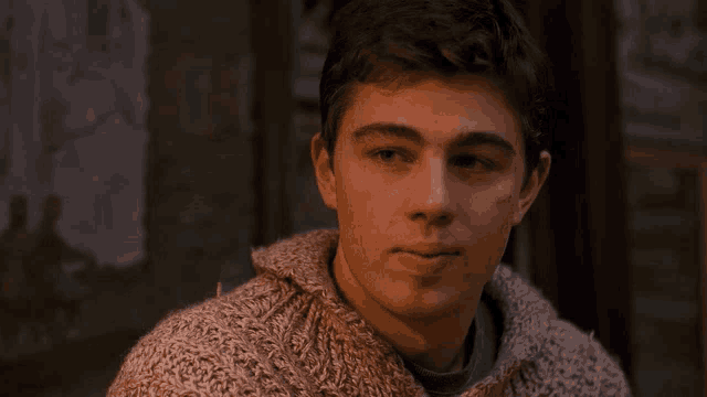 a young man in a sweater looks at the camera with a serious look on his face