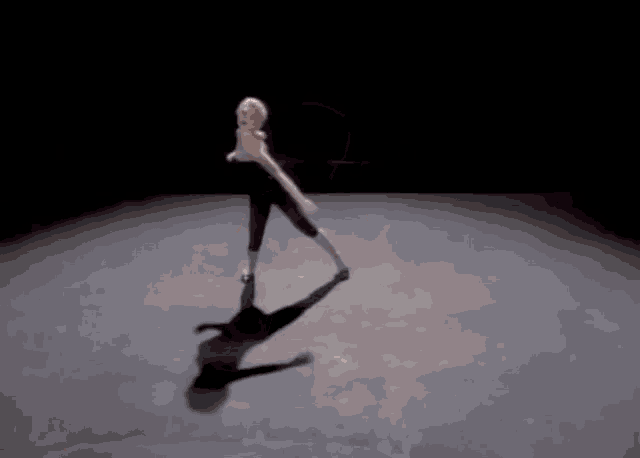 a woman is dancing in a dark room with a shadow on the floor .