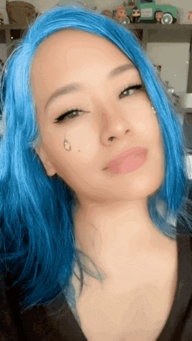 a woman with blue hair has a tattoo on her face