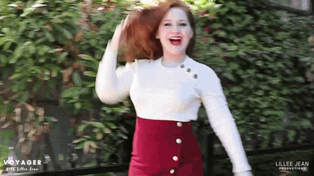 a woman wearing a white sweater and a red skirt is standing in front of a fence with the words voyager on the bottom