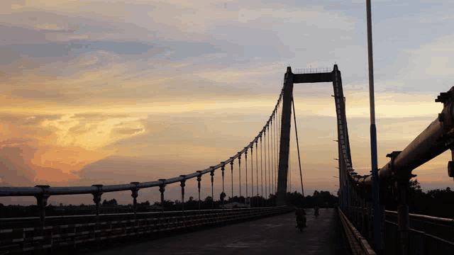 a bridge with a sunset in the background and a person riding a bike