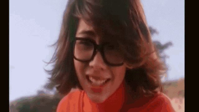 a close up of a woman wearing glasses and an orange shirt .
