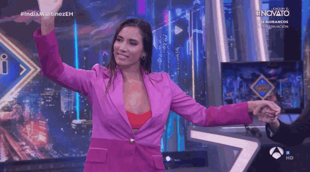 a woman in a pink jacket is dancing in front of a screen that says novato on it