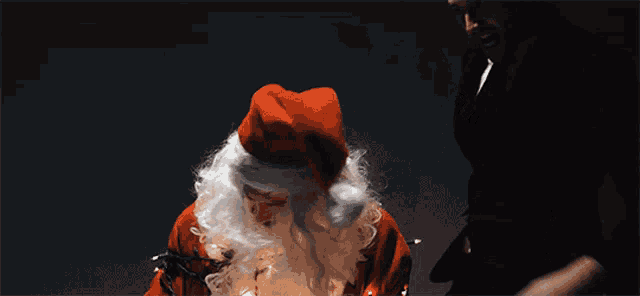 a man in a black suit stands next to a man dressed as santa