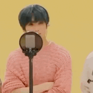 a boy in a pink sweater is standing in front of a microphone .