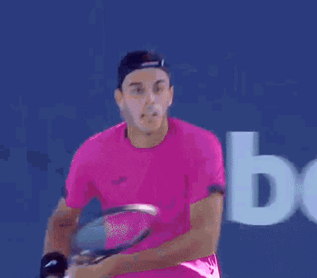 a man in a pink shirt is holding a tennis racquet in front of a sign that says itaú .