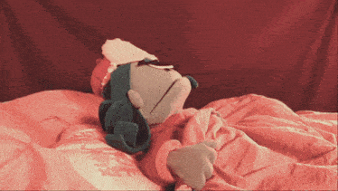 a stuffed animal is laying on a bed with a red blanket