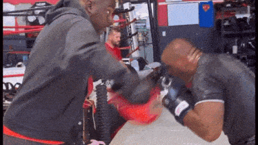 two men are boxing in a gym and one of them is wearing a shirt that says ' superman '