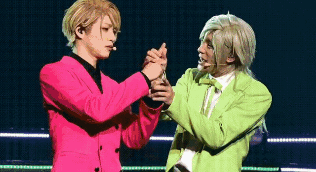 a man in a pink jacket and a man in a green jacket are holding hands on a stage .