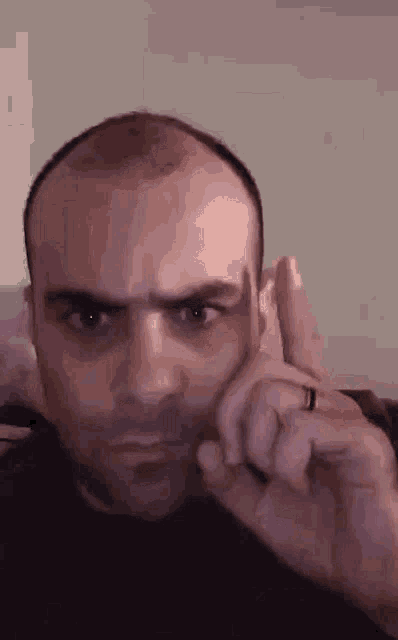 a man with a ring on his finger is making a funny face while holding his finger to his ear .