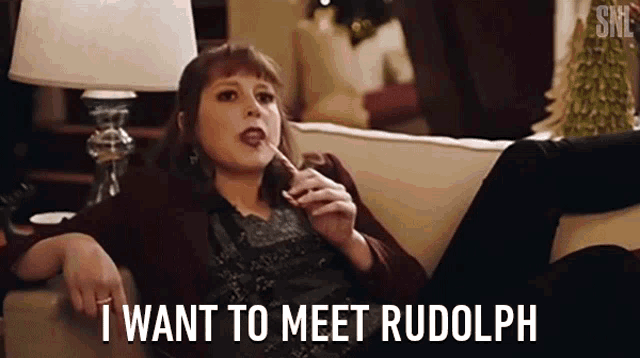 a woman is sitting on a couch eating a lollipop and says i want to meet rudolph .