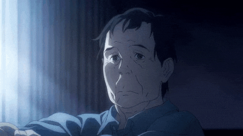 a man in a blue shirt is sitting in front of a window and looking at the camera .
