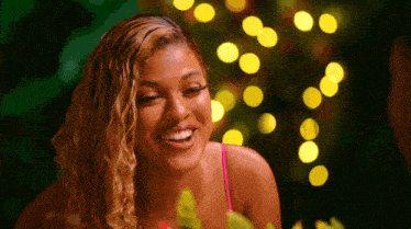 a woman in a pink tank top smiles in front of a christmas tree