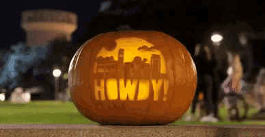 a pumpkin with the word howdy carved into it is sitting on a sidewalk .