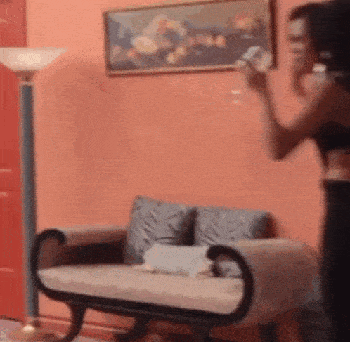 a woman is standing next to a couch in a living room holding a bottle of water .