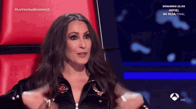 a woman is sitting in a chair with her hands outstretched in front of a screen that says la voz audiciones 2