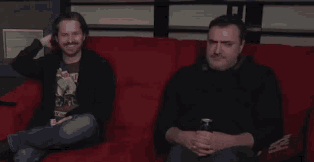 two men are sitting on a red couch and one of them has a shirt that says ' metallica ' on it