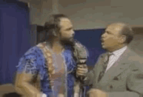a man in a suit is holding a microphone and talking to another man in a room .