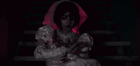 a woman in a bloody wedding dress is holding her hands over her heart .