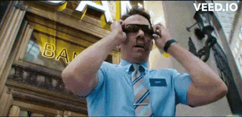 a man in a blue shirt and tie is adjusting his sunglasses in front of a bank .