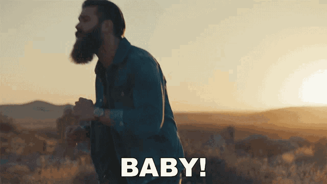 a man with a beard is standing in the desert and the word baby is written below him