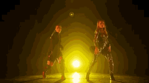 a couple of women are dancing in front of a yellow light