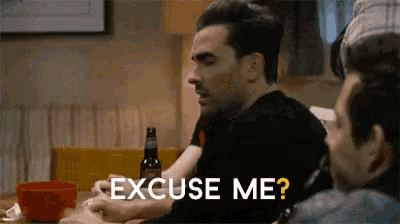 a man is sitting at a table with a bottle of beer and says " excuse me "