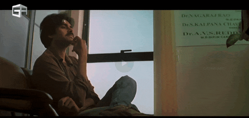 a man sits in front of a window with a sign on the wall that says dr.a.v.s.reddy