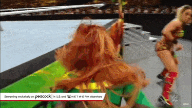 two women are wrestling on a wrestling ring and one of them is wearing a green outfit .