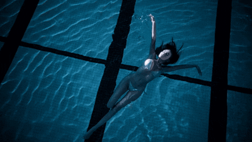 a woman in a bikini is swimming in a dark pool