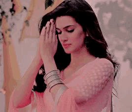a woman in a pink saree is praying with her hands folded .
