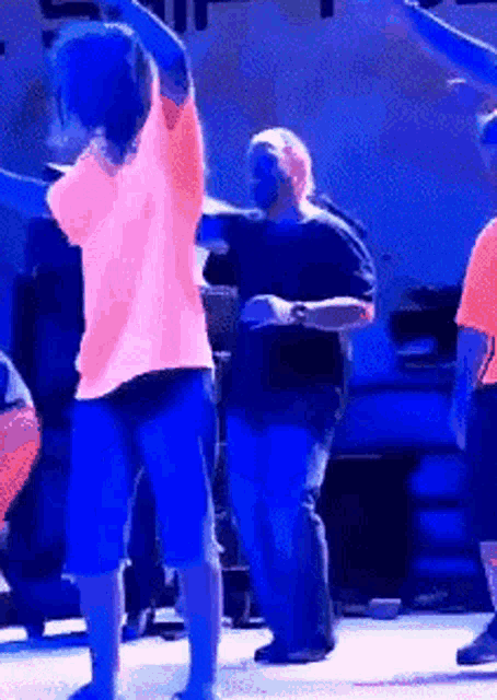 a woman in a neon pink shirt is dancing on a stage with other people