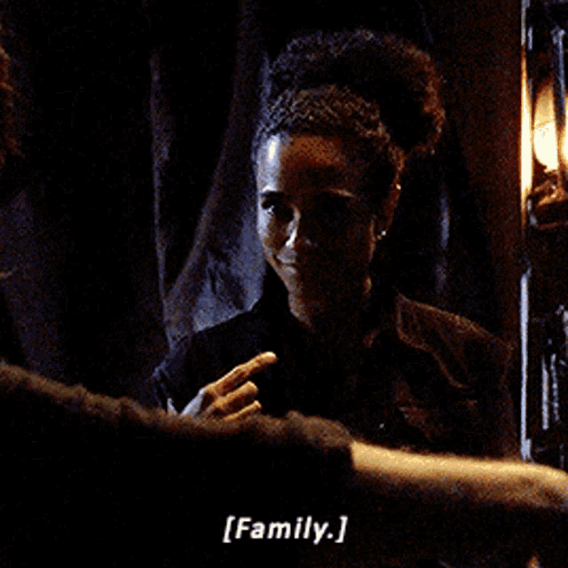 a woman in a dark room is holding her hands up and says family