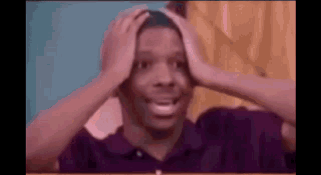 a man in a purple shirt is holding his head and making a surprised face .
