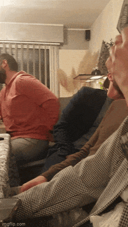 a group of men are sitting on a couch and one of them is wearing a red hoodie