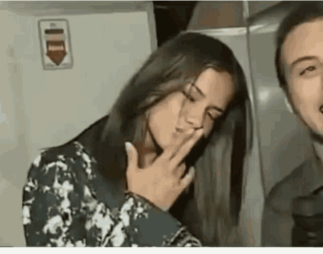 a woman is covering her mouth with her hand while a man is standing next to her .