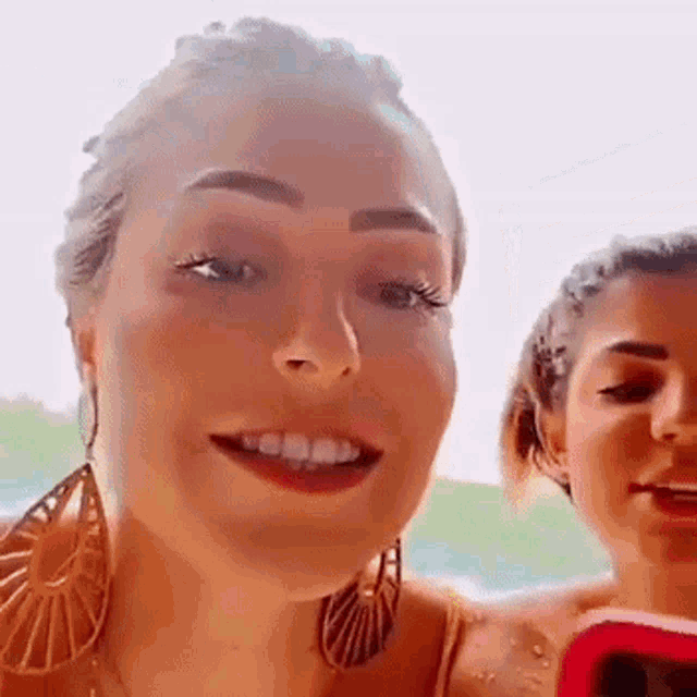 a woman wearing earrings is smiling while another woman holds a cell phone .